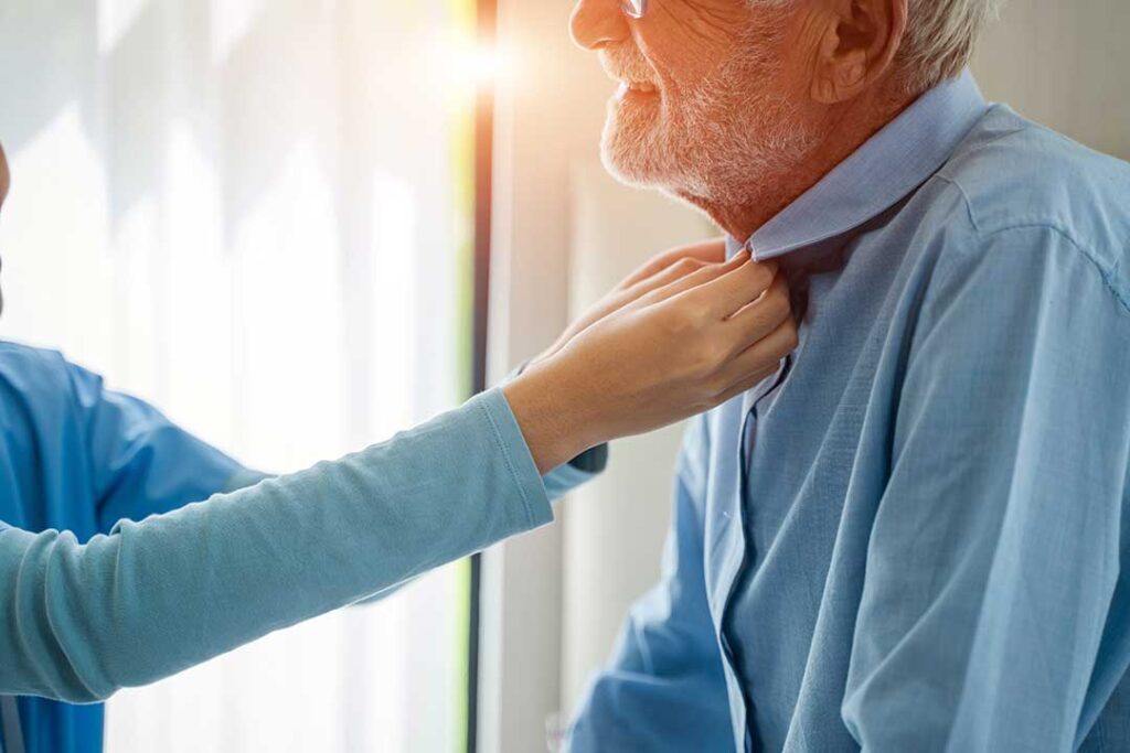 A senior resident and caregiver practicing hand hygiene together at a communal sink in a residential facility.