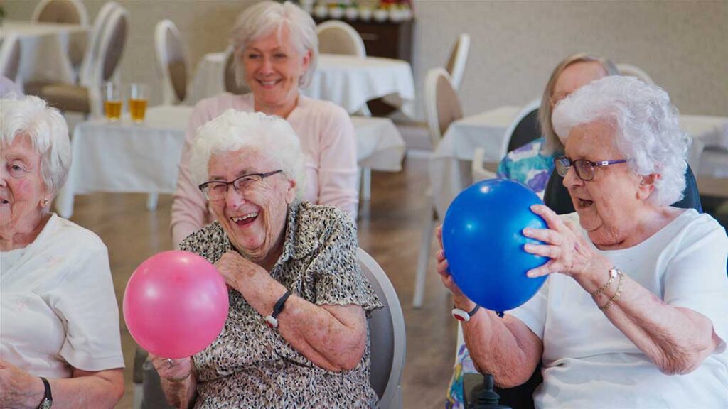 Older LGBTQ+ adults and staff member having a respectful conversation in a bright assisted living common room.