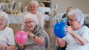 Older LGBTQ+ adults and staff member having a respectful conversation in a bright assisted living common room.